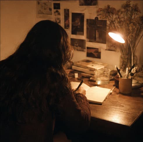 A woman writing at a warm desk late at night